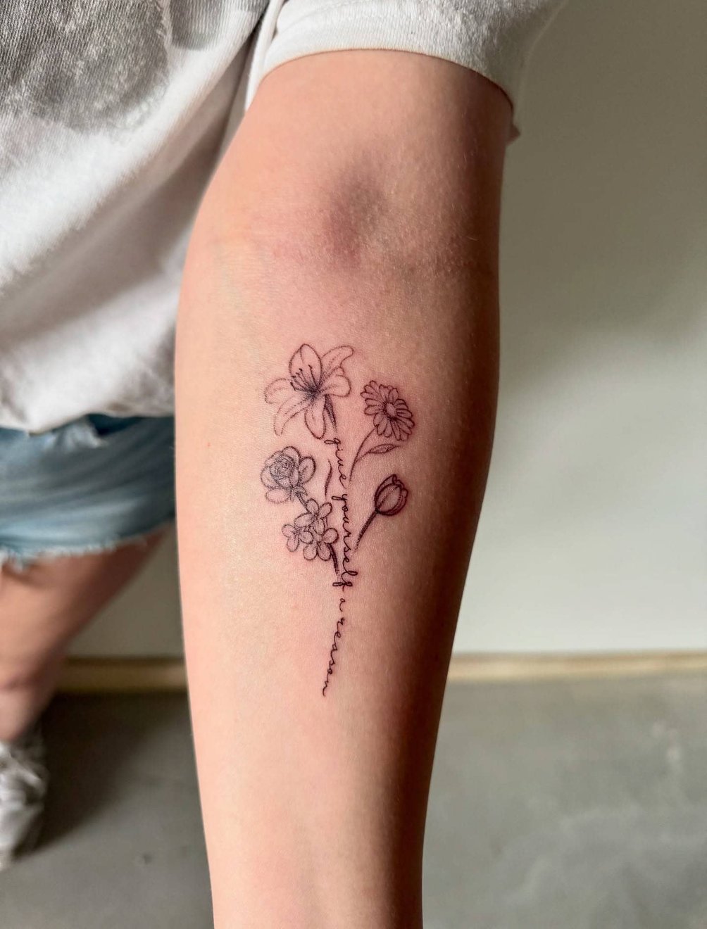 Delicate fine line floral tattoo on a forearm